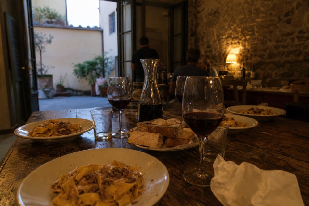 A table set with plates of fresh pasta, glasses of red wine and rustic bread, no text, no logos, no people