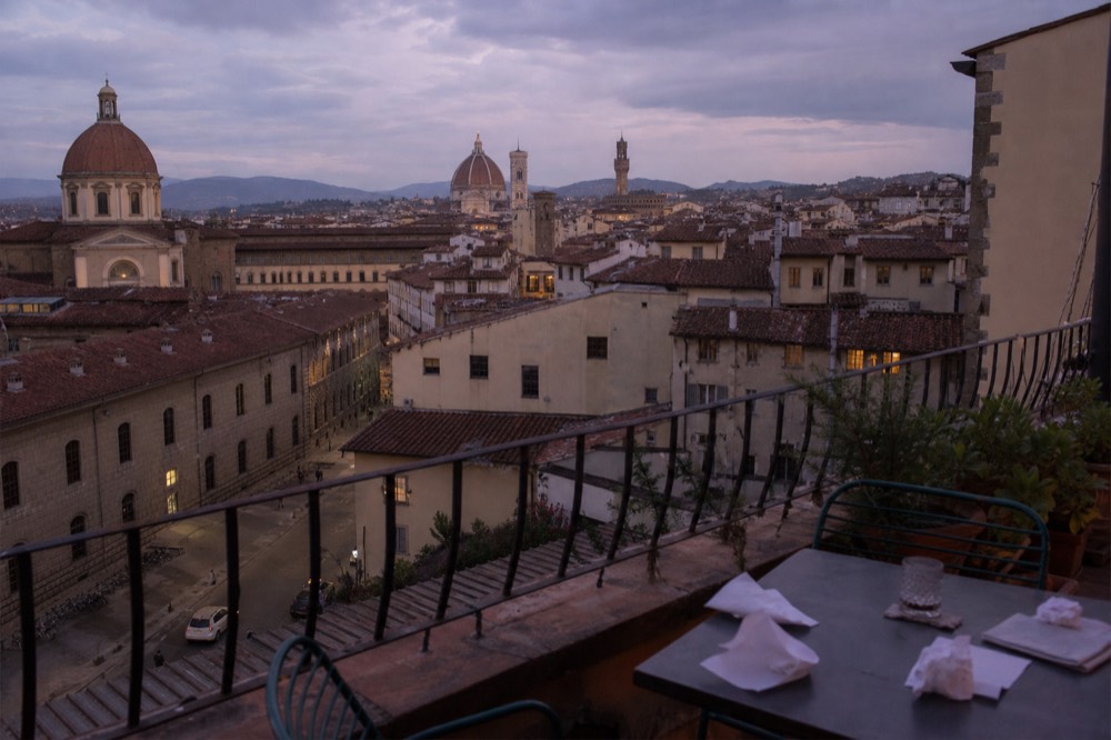 Rooftop terrace at dusk overlooking Florence rooftops and the Duomo, no text, no logos, no people