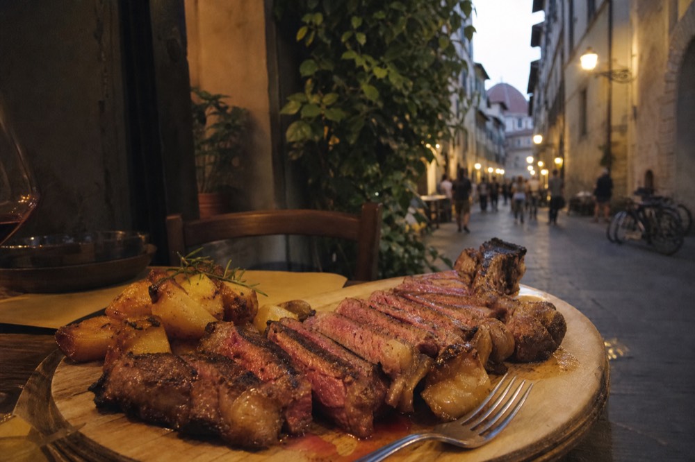 Sliced Florentine T-bone steak on a wooden board with roast potatoes, no text, no logos, no people
