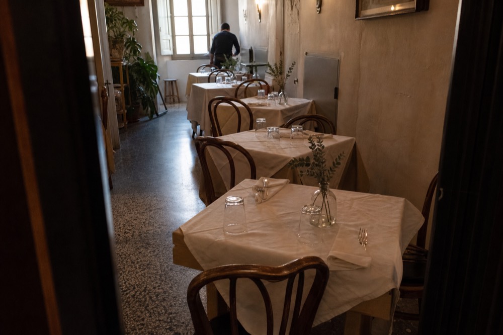 A narrow Florentine dining room with tables close together before service, no text, no logos, no people