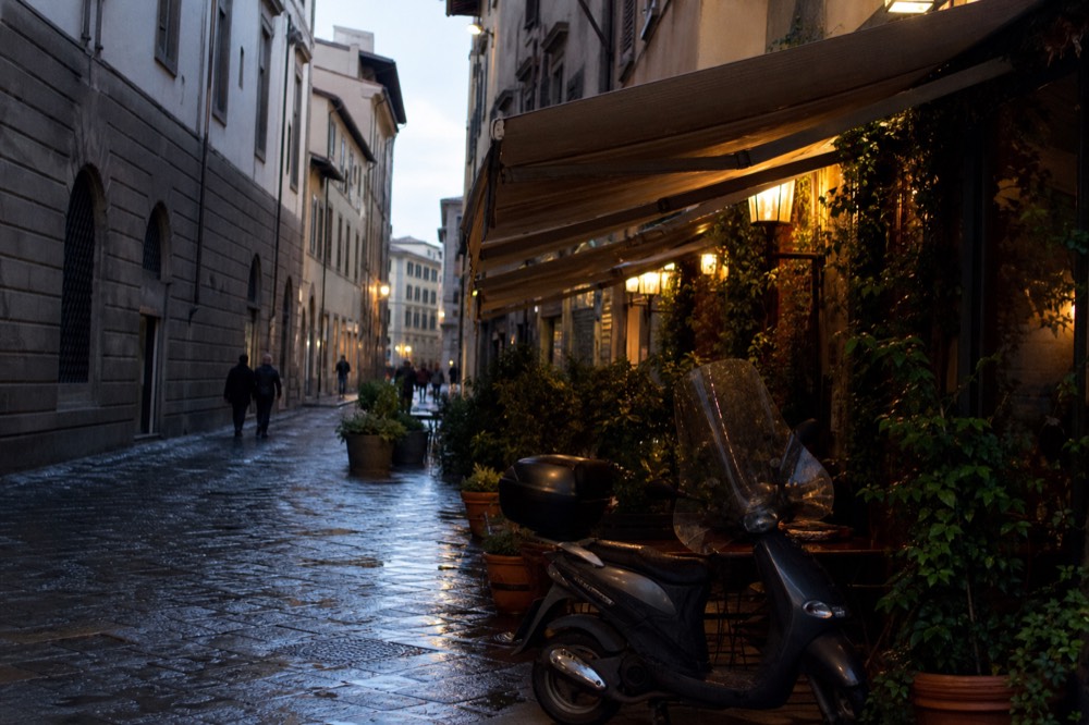 A Florentine street at dusk with restaurant awnings and lit windows, no text, no logos, no people