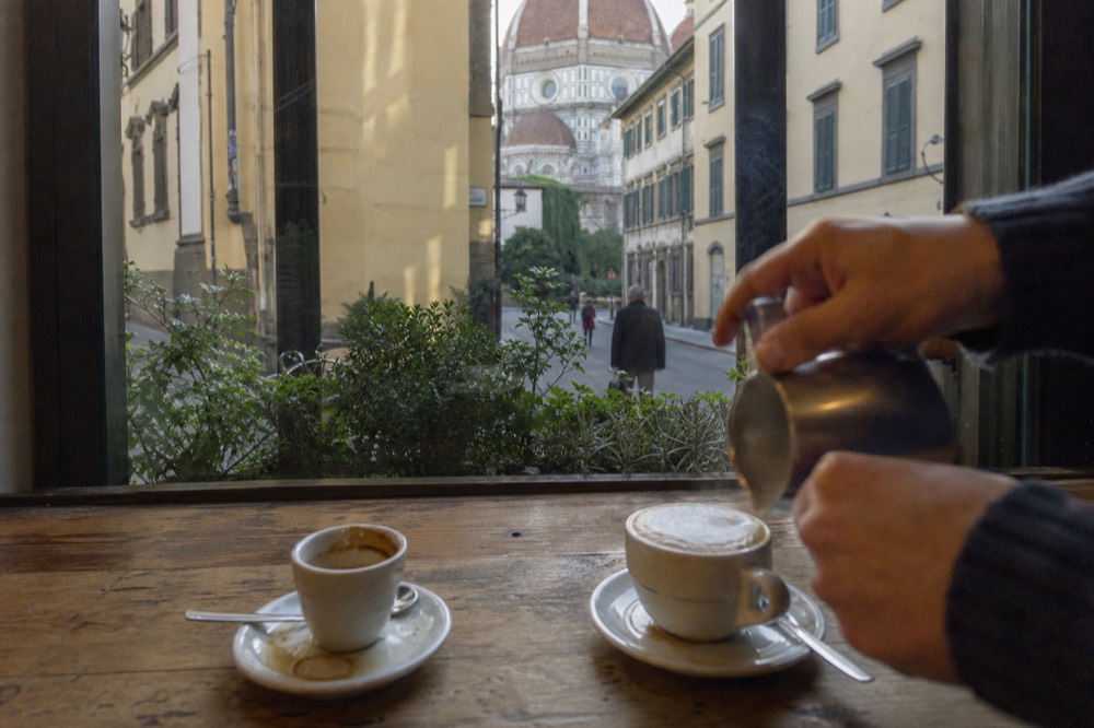 A barista's hands finishing a cappuccino with foam on a wooden bar top, no text, no logos, no people