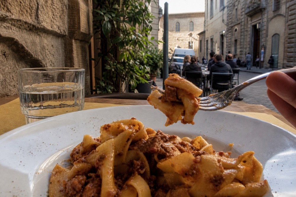 A plate of fresh pappardelle pasta with duck ragu on a small trattoria table in Florence, no text, no logos, no people