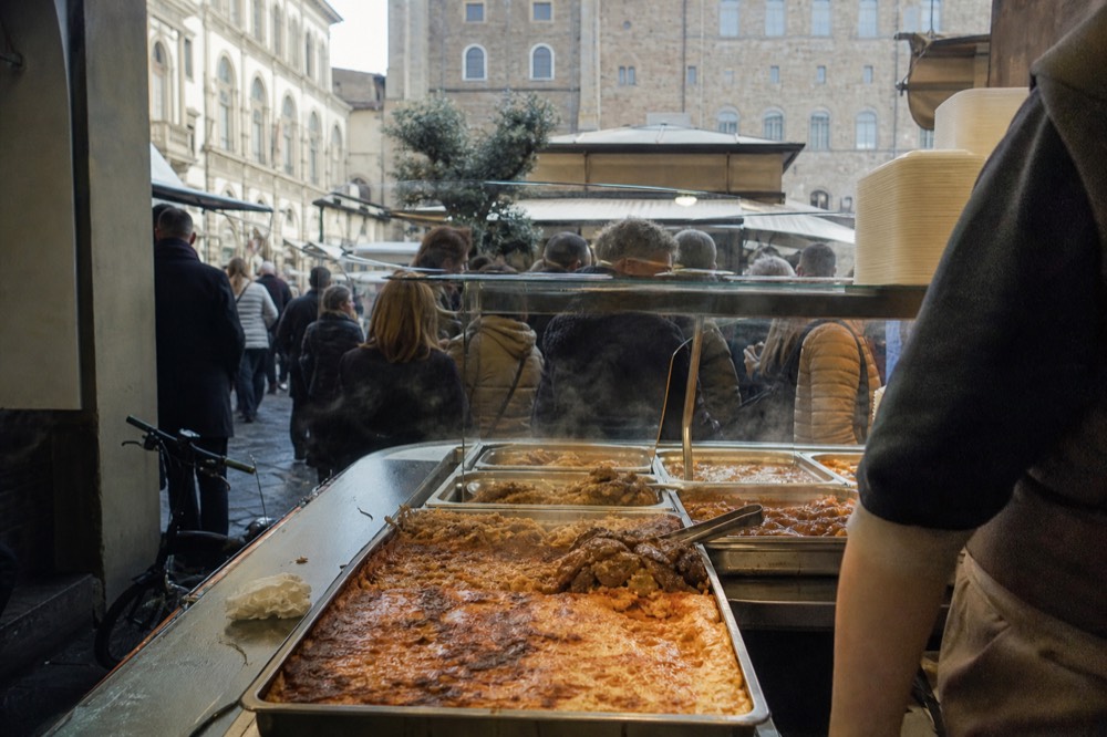 A bustling Florentine food market stall with trays of ready dishes at lunchtime, no text, no logos, no people