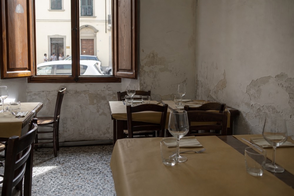 A small trattoria dining room with simple wooden tables set for lunch, no text, no logos, no people