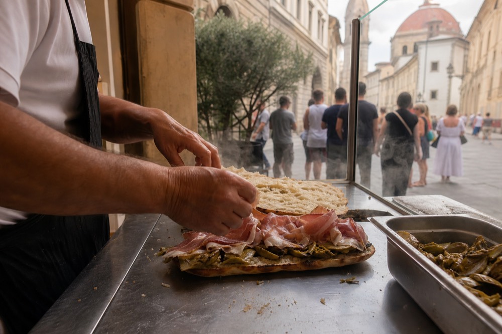 A schiacciata sandwich being assembled at a Florence deli counter, no text, no logos, no people
