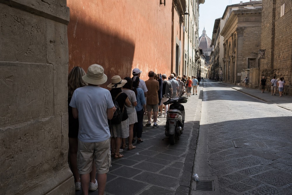 A line of people waiting outside a sandwich shop on a Florence street, no text, no logos, no people