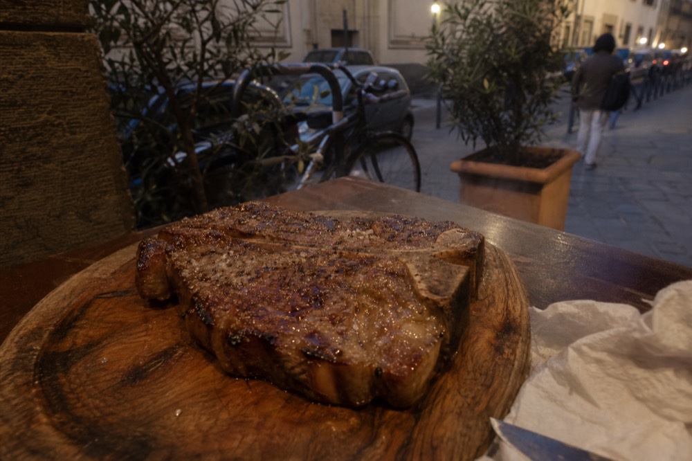 A thick grilled T-bone steak resting on a wooden board in a Florence restaurant, no text, no logos, no people