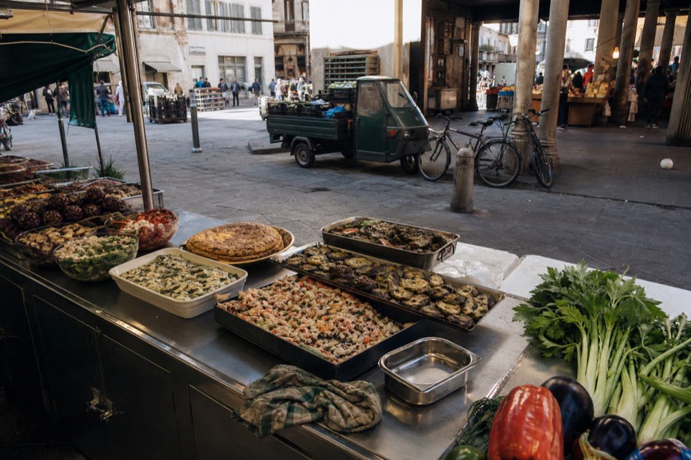 A stainless-steel market counter loaded with fresh produce and prepared dishes, no text, no logos, no people