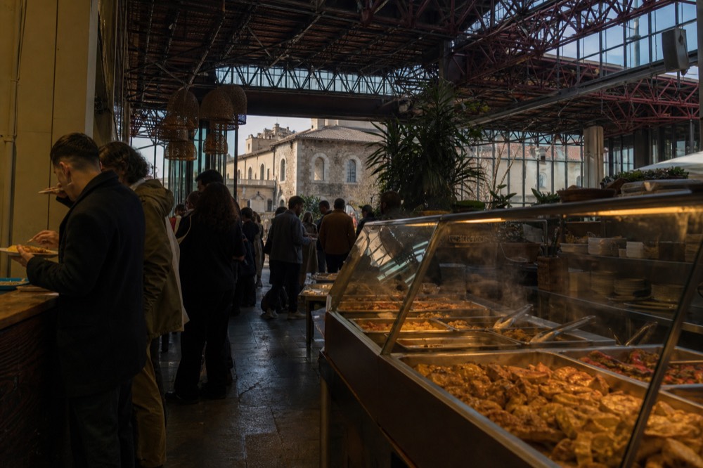 A market food counter with trays of ready dishes and customers standing, no text, no logos, no people
