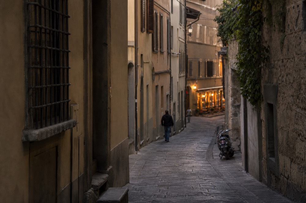 A narrow Florence street in early evening light with stone buildings and distant restaurant lights, no text, no logos, no people