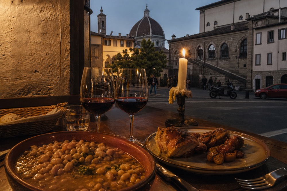 A candlelit trattoria table with wine glasses and Tuscan dishes set for an evening meal, no text, no logos, no people