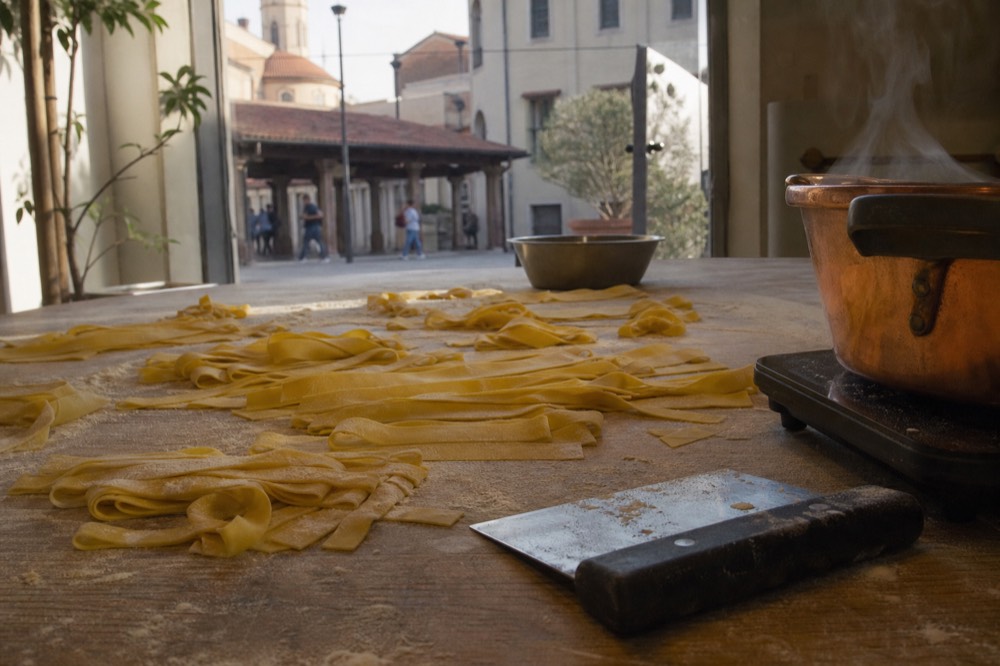 Hands cutting fresh tagliatelle strips on a wooden table with flour, no text, no logos, no people