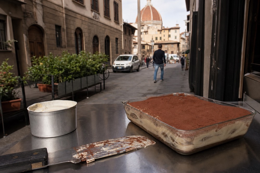 A glass dish of freshly assembled tiramisu with cocoa powder on top, no text, no logos, no people