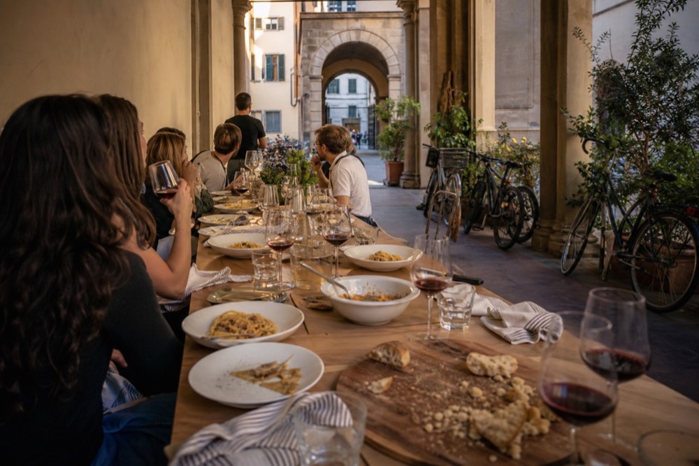 A long shared table set with plates of pasta and glasses of wine, no text, no logos, no people