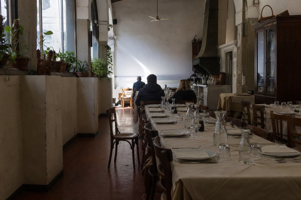 A Florence trattoria dining room with shared tables set for lunch service, no text, no logos, no people