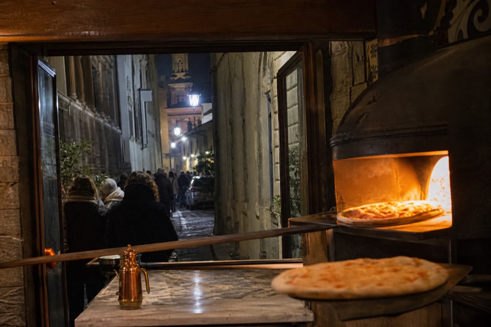 A pizzeria counter in Florence with pizzas coming out of an oven at night, no text, no logos, no people