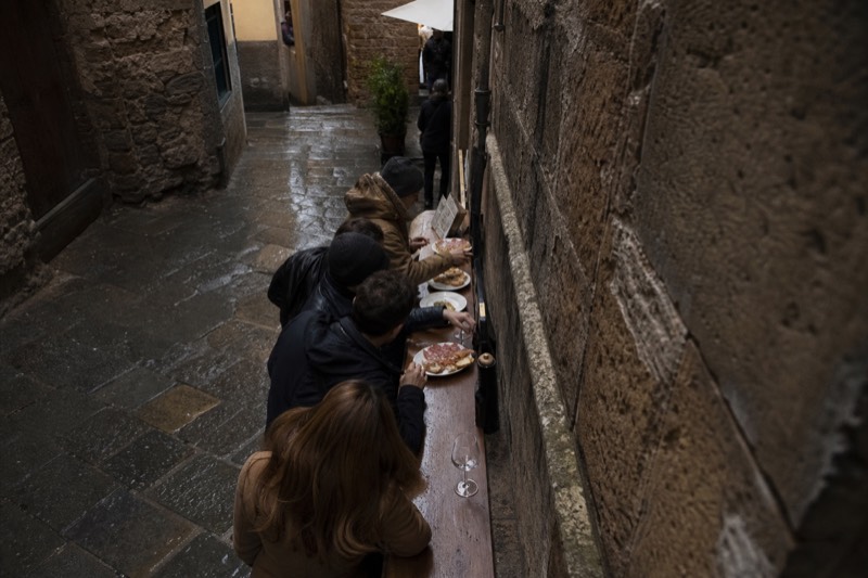 A small group of walkers gathered at a Florence street corner tasting crostini and cured meats from paper plates, a guide holding up a glass of wine, medieval stone buildings rising close behind them