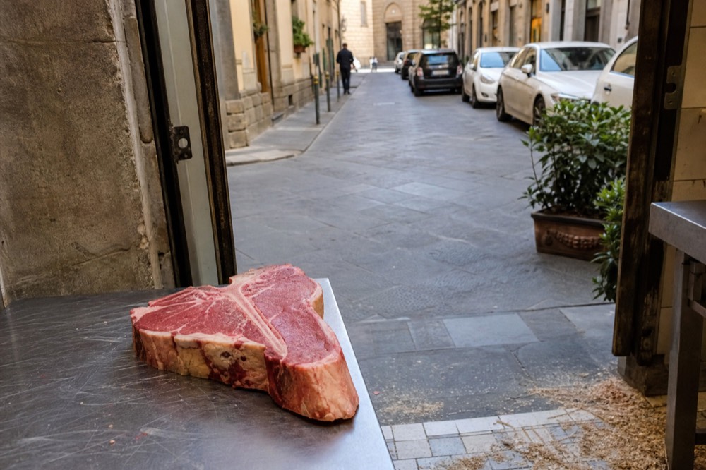 A thick raw T-bone steak with fillet and sirloin on either side of the bone on a butcher's counter, no text, no logos, no people