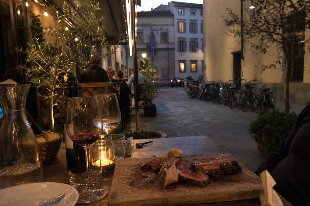 A steakhouse bill beside a partly eaten bistecca on a wooden board, no text, no logos, no people