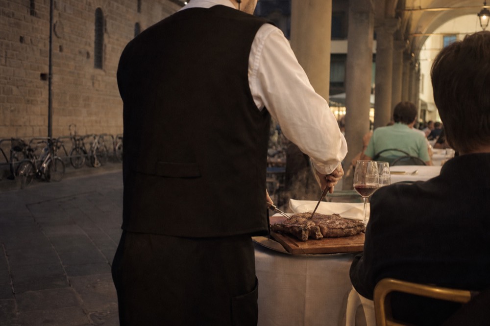 A waiter carving a grilled T-bone steak at a restaurant table, no text, no logos, no people