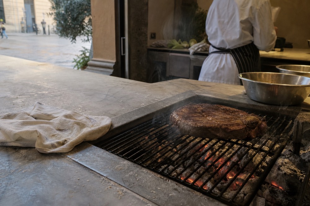 A cooking class kitchen with a thick steak over charcoal embers, no text, no logos, no people