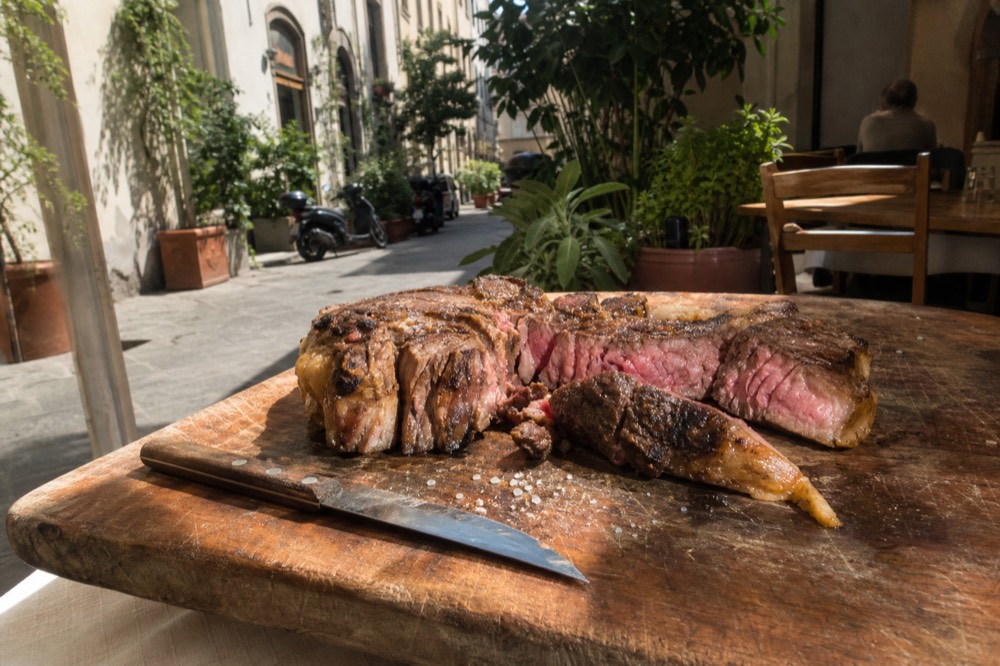 A grilled bistecca alla fiorentina sliced open showing a rare pink interior on a rustic board, no text, no logos, no people