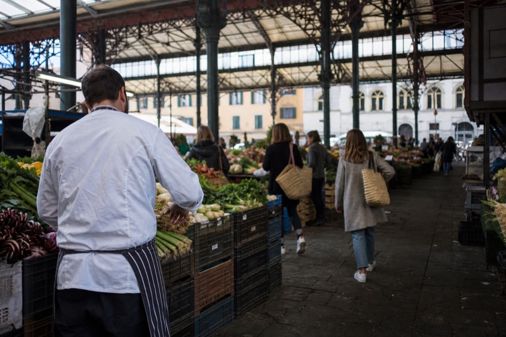 A chef and shoppers at a covered market produce stall selecting vegetables, no text, no logos, no people
