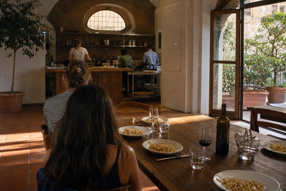 A long wooden table set with wine glasses and plates of fresh pasta ready for a meal, no text, no logos, no people