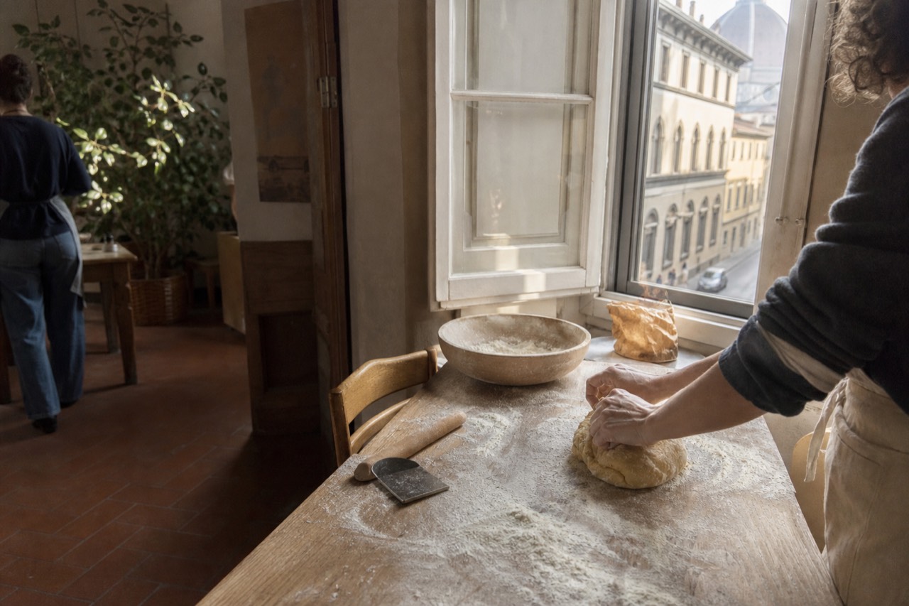 Hands kneading fresh pasta dough on a floured wooden table in a Florence kitchen, no text, no logos, no people