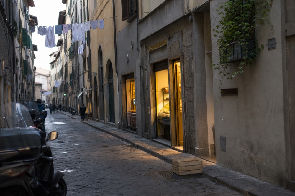 A narrow Florence street with food shops and counters, no text, no logos, no people