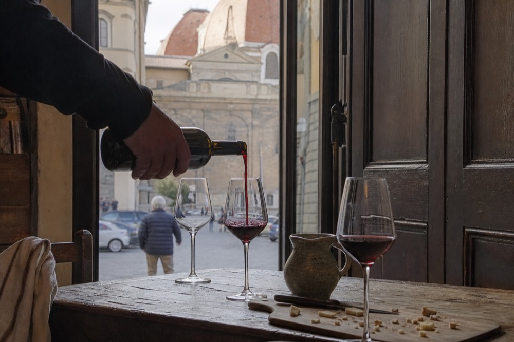 A sommelier pouring red wine into glasses on a rustic wooden table, no text, no logos, no people