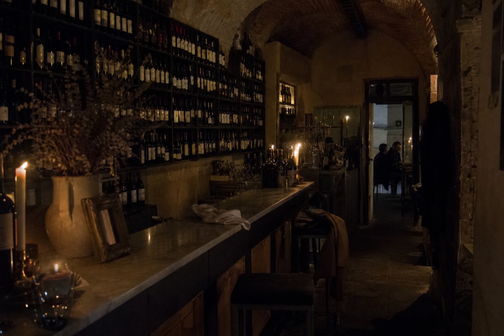 A dark wine bar interior with bottles racked to the ceiling, no text, no logos, no people