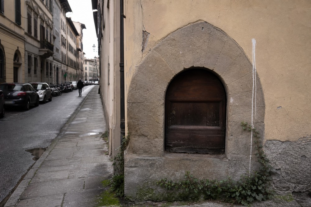 A restored arched wine window with a small wooden door in a Florence palace wall, no text, no logos, no people