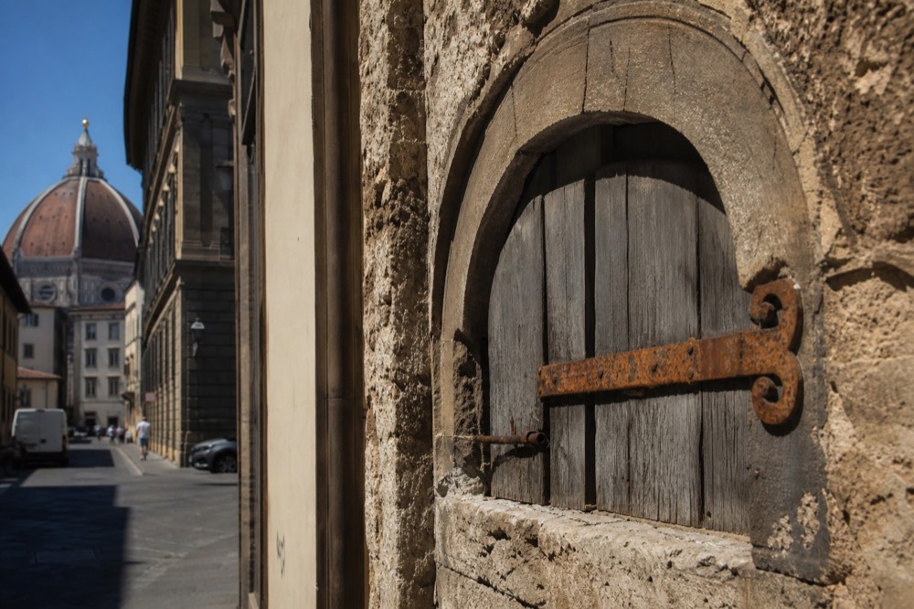 A close view of an arched stone opening with a weathered wooden shutter in an old Florence facade, no text, no logos, no people