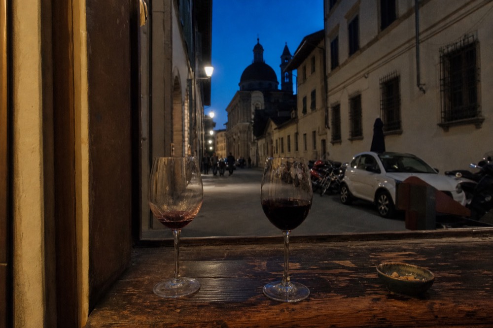 Glasses of Tuscan red wine on a wooden counter in a dimly lit enoteca, no text, no logos, no people