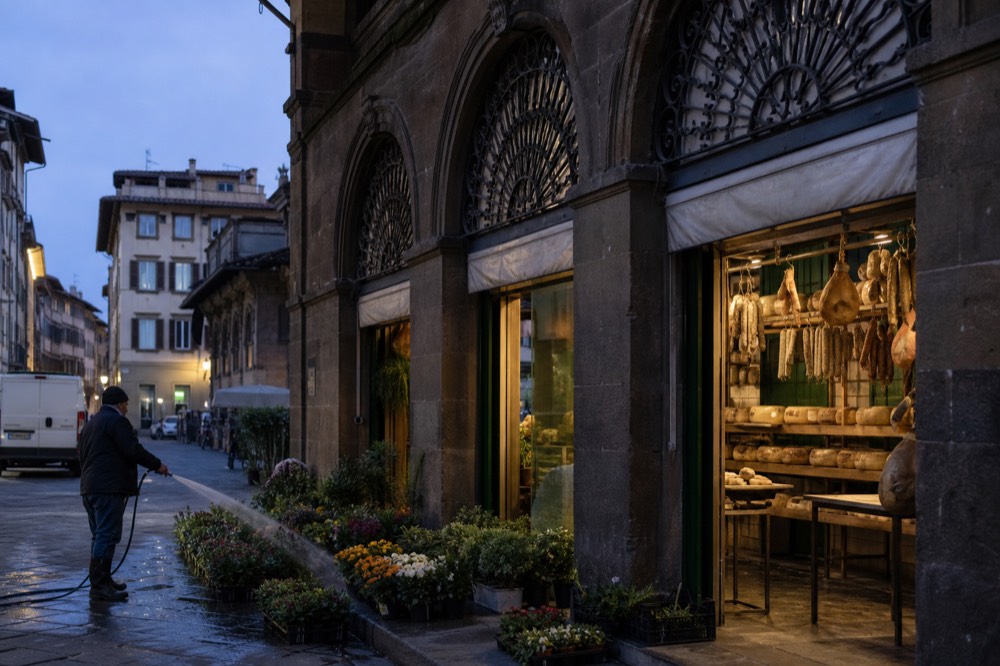 Early morning pecorino wheels and salumi behind wrought-iron arcade at Sant'Ambrogio market, damp cobbles, no text, no logos, no people