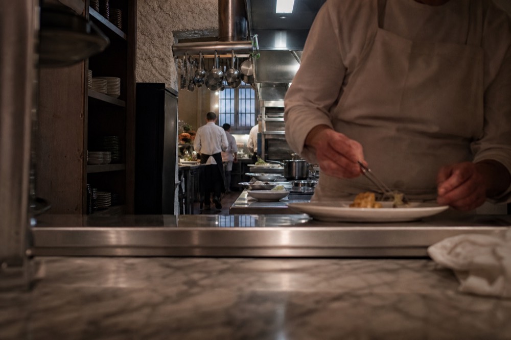 Chef plating a refined course on a marble kitchen pass, no text, no logos, no people