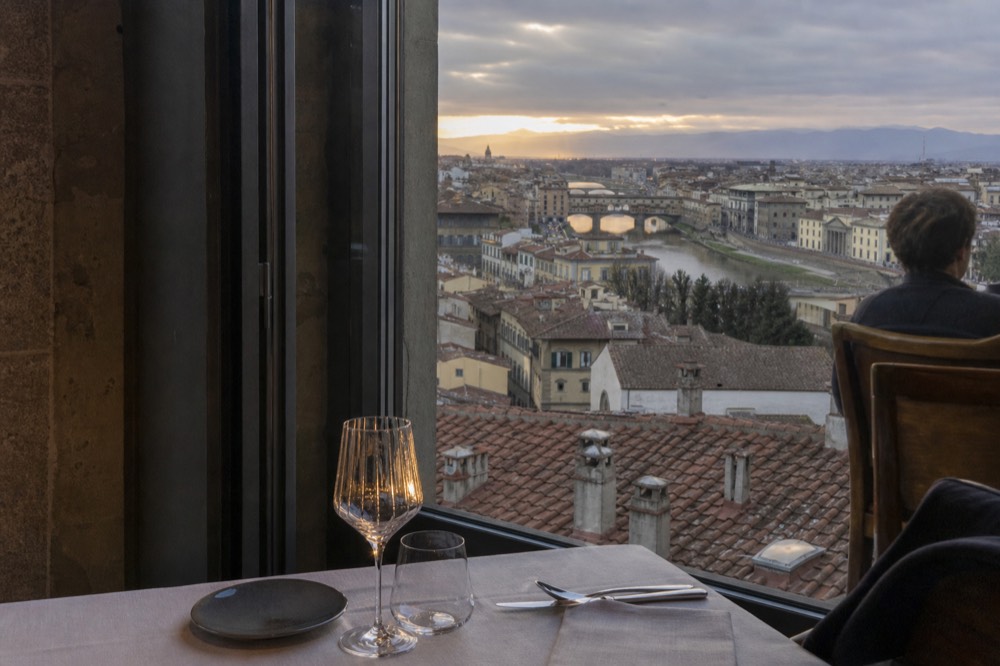 Set fine dining table beside a window overlooking Florence rooftops at dusk, no text, no logos, no people