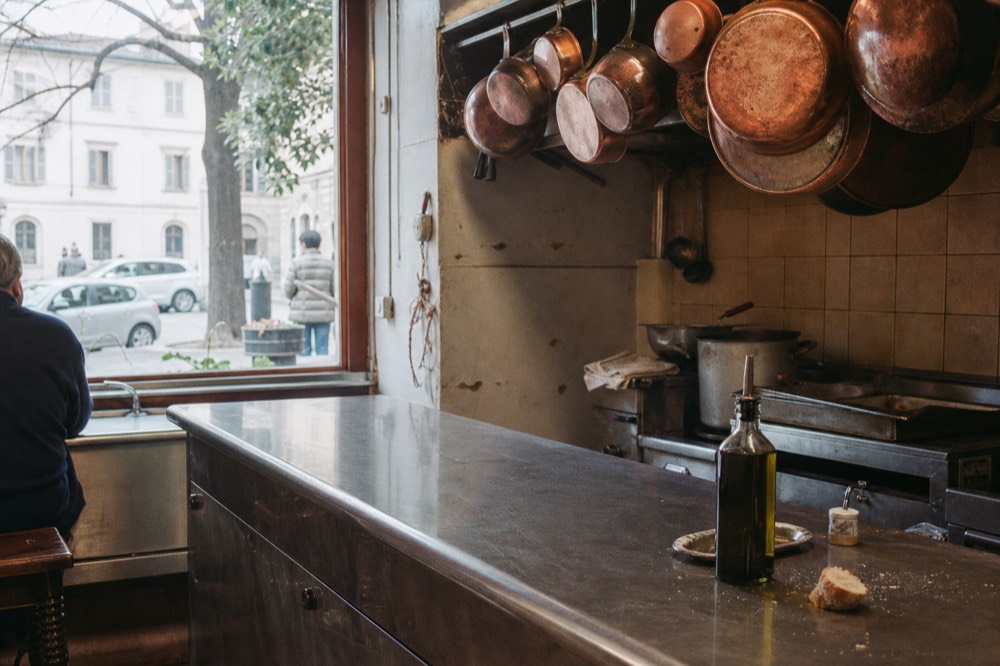 Simple trattoria counter with handwritten menu board and copper pans, no text, no logos, no people
