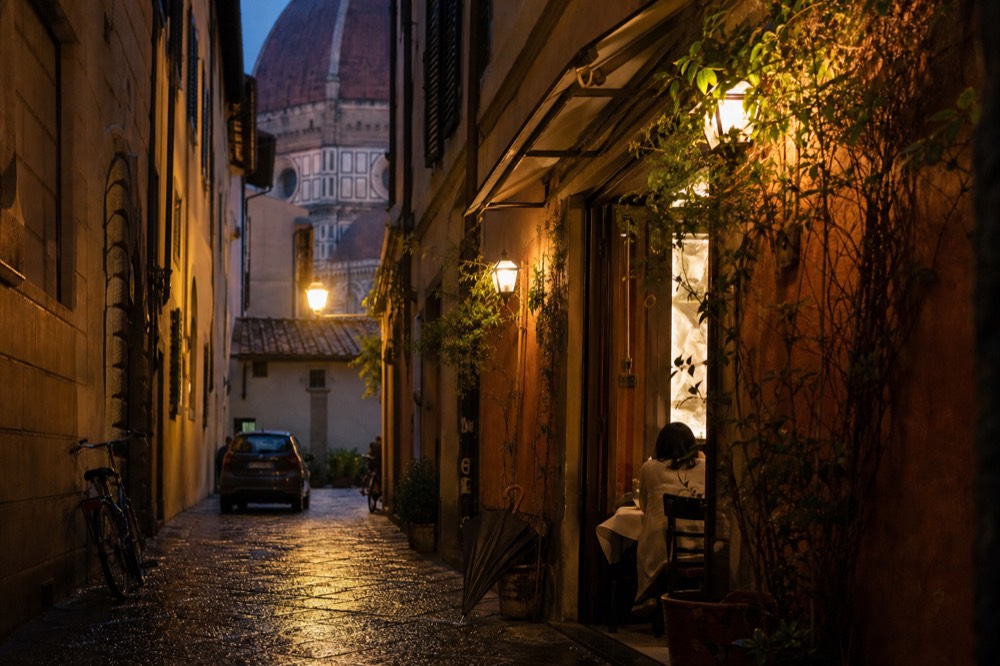 Evening view of a lit Florence restaurant entrance on a narrow street, no text, no logos, no people