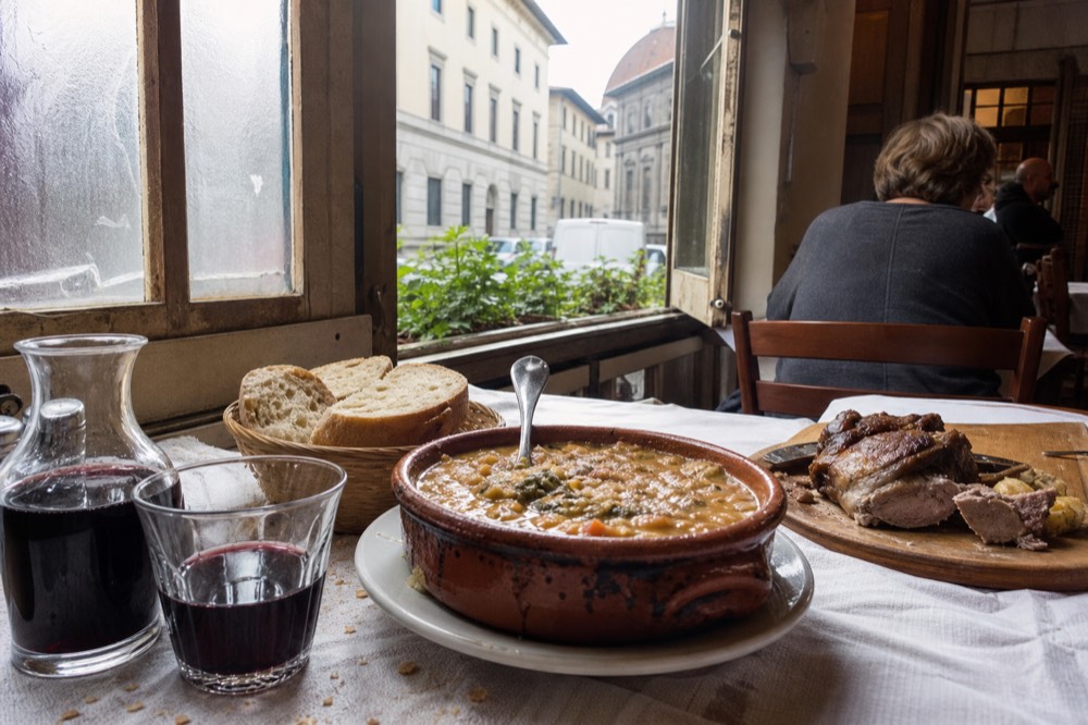 A spread of Tuscan dishes including ribollita, bread and roasted meat on a wooden table, no text, no logos, no people