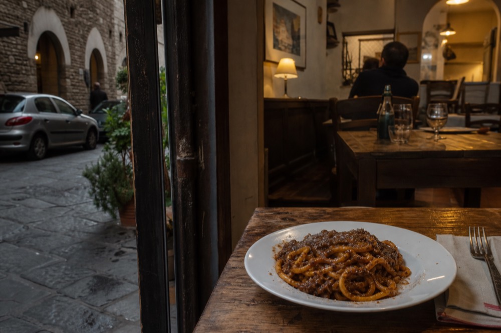 A plate of thick hand-rolled pici pasta with meat sauce, no text, no logos, no people