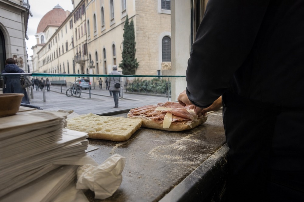 A flat focaccia bread being split and filled with cured meats on a counter, no text, no logos, no people