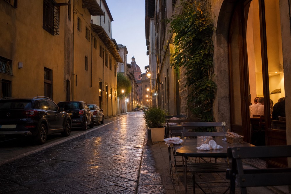 A Florentine street in the evening with restaurant lights along the pavement, no text, no logos, no people