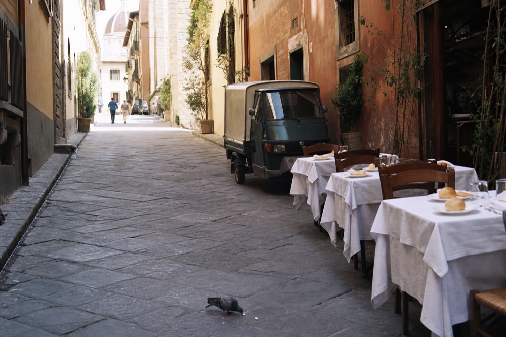 Old Florentine street with trattoria tables set for lunch, no text, no logos, no people