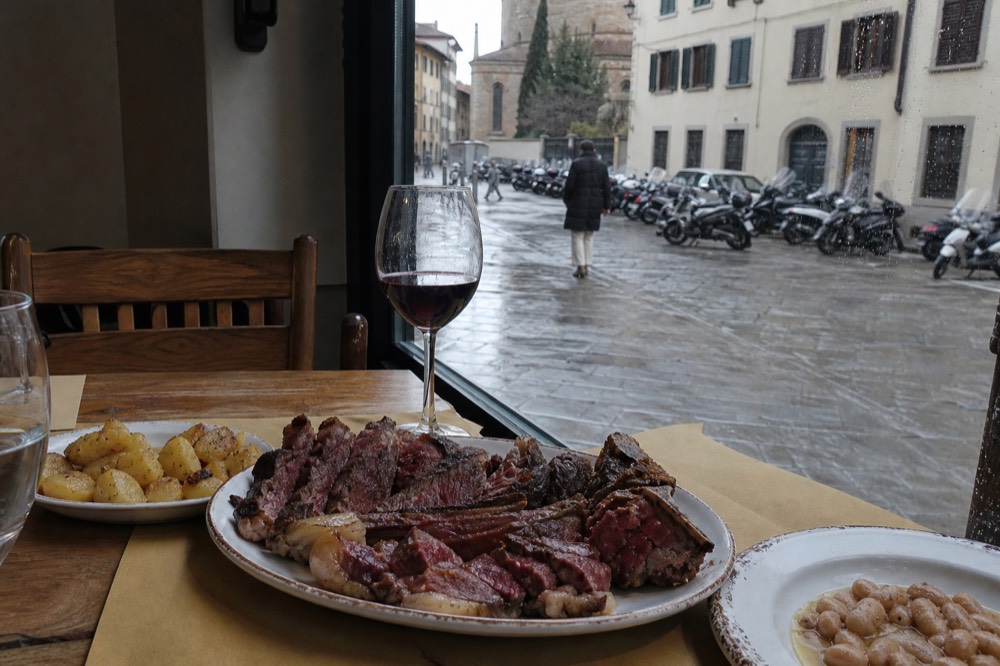 Florentine steak and side dishes on a trattoria table, no text, no logos, no people