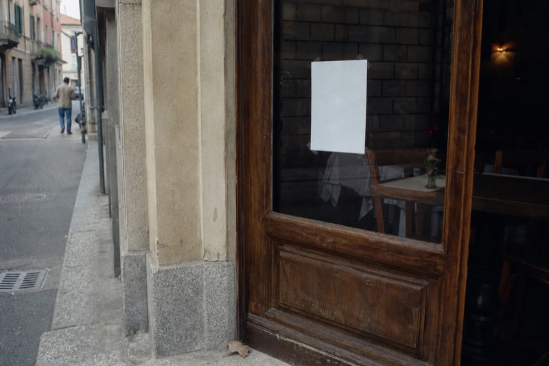 A Florence trattoria door with its printed opening hours and closing day taped inside the glass, the dining room dark behind it