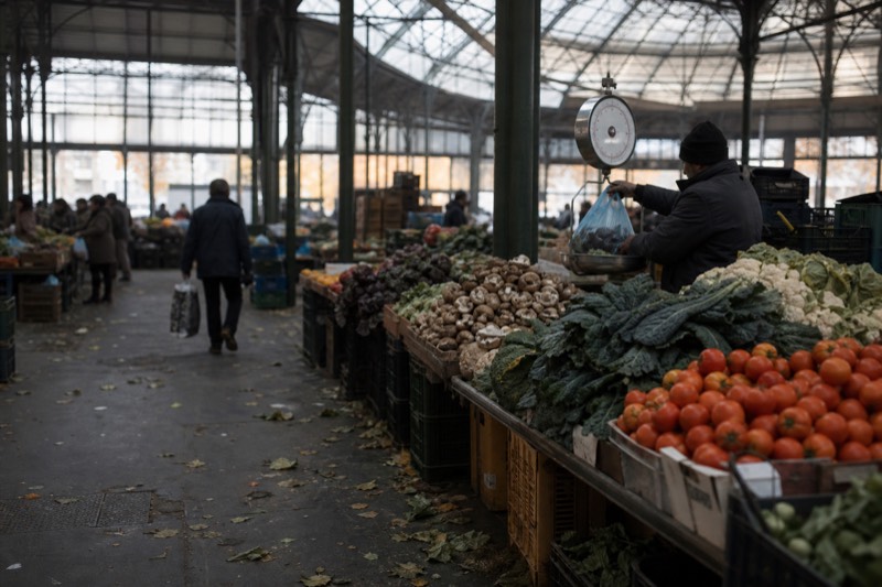 A produce stall inside the Mercato Centrale in Florence stacked with tomatoes, cavolo nero and porcini, a vendor weighing an order at the scale