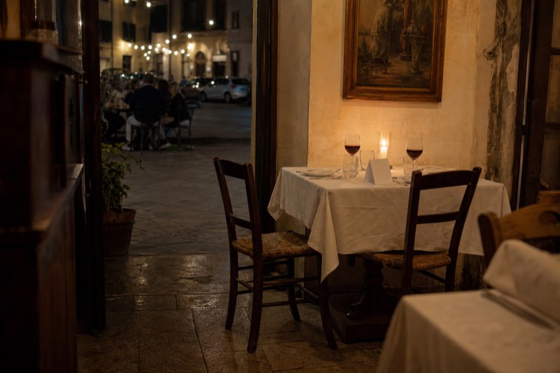 A table laid for a booked dinner in a Florence dining room at night, two empty chairs pulled out, glasses poured and a reserved card standing on the cloth